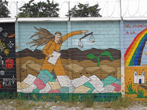 A wall mural in Guatemala depicts a blind Justice figure reviewing documents.